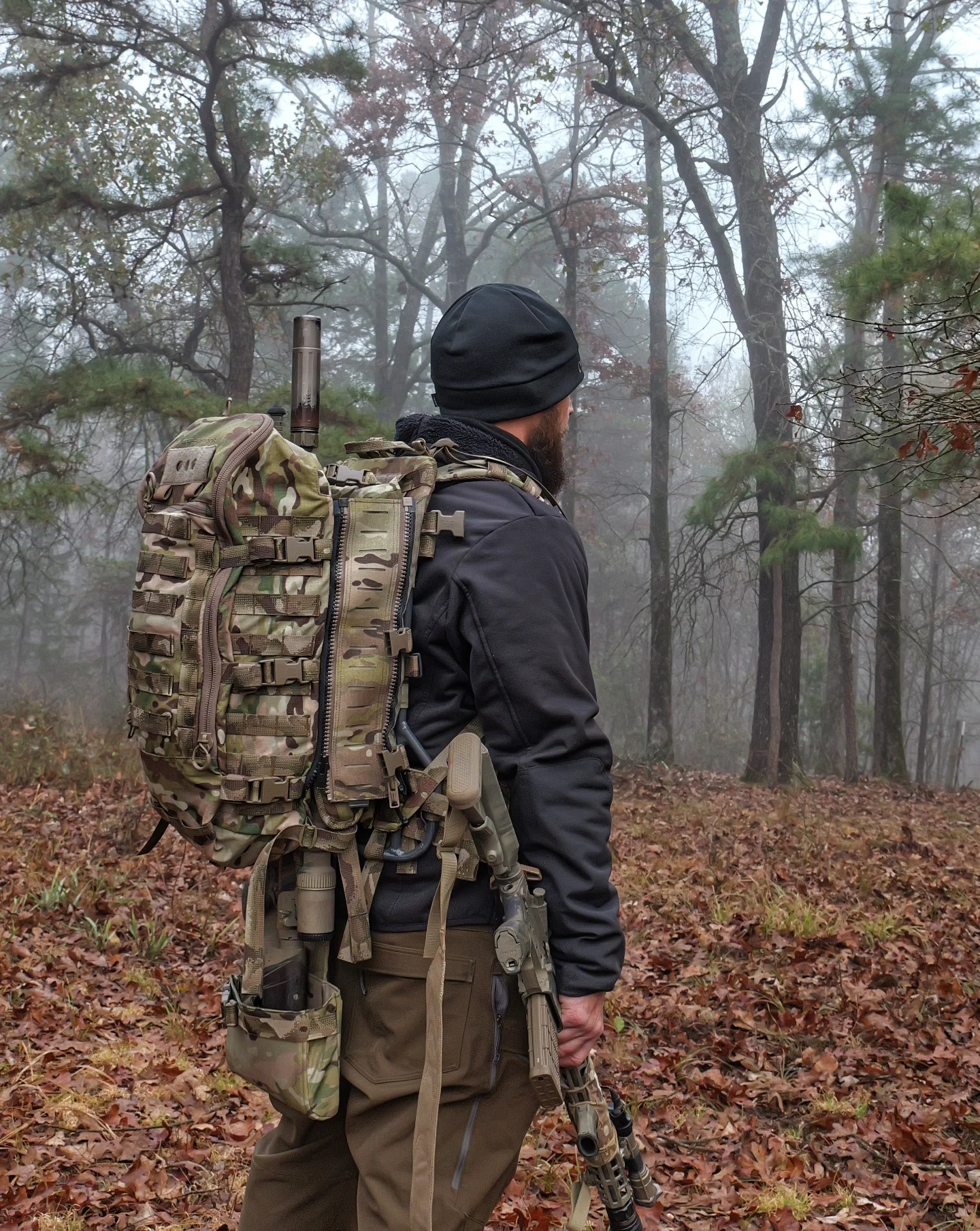 Hunter shouldering Eberlestock multicam pack with slung rifle in foggy oak timber