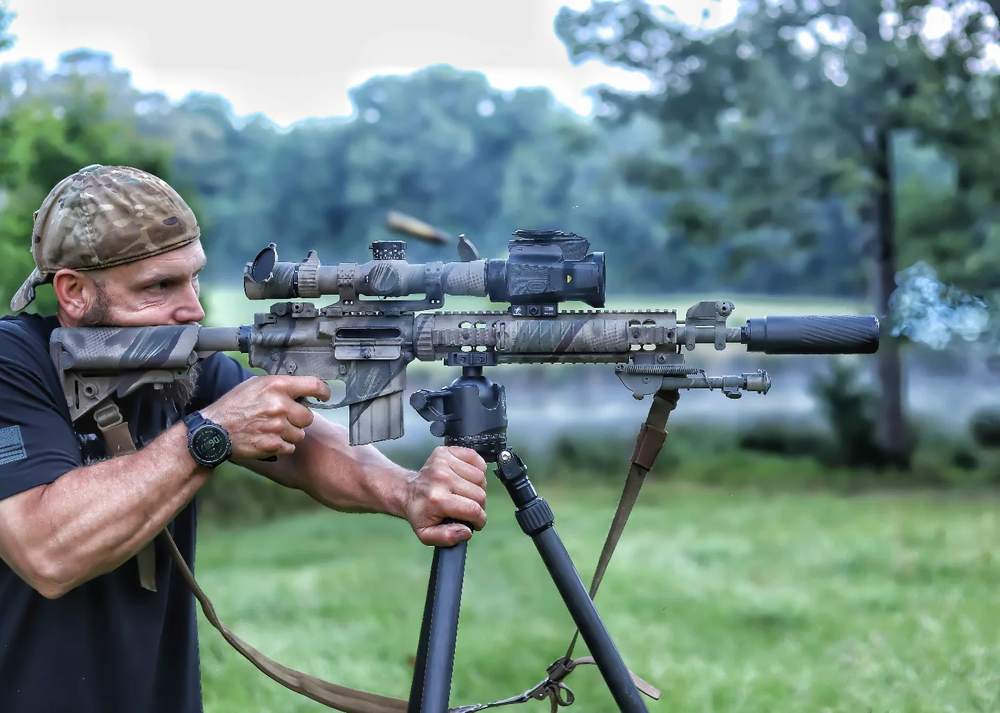 Tripod shooting position with TBAC suppressor, brass in air